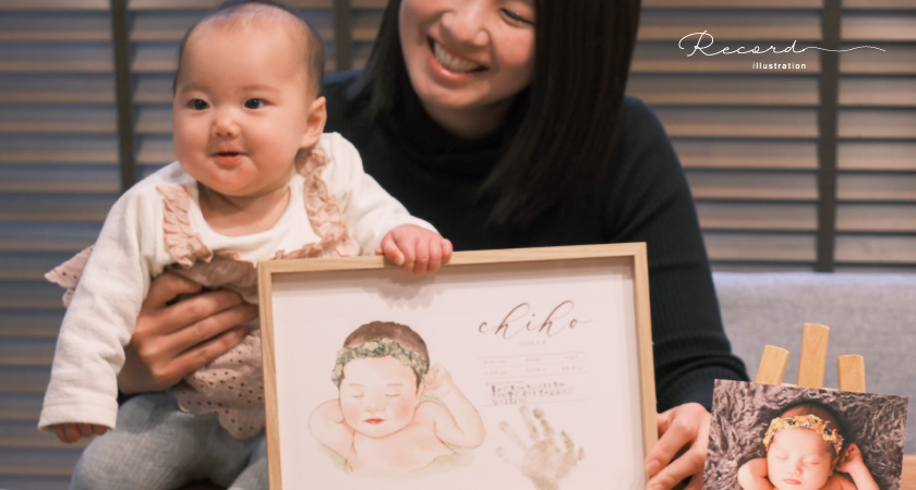 ご家族が手形を押したあとの似顔絵入り命名書を、お母さんと赤ちゃんが持っているところ